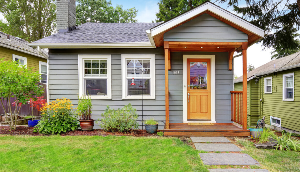 shutterstock_217685257 Small grey house with wooden deck. Front yard with flower bed and lawn